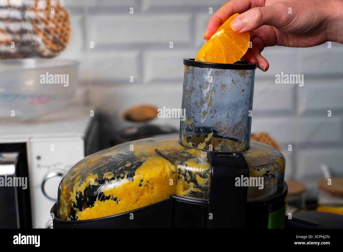 Primo piano della centrifuga elettrica che estrae il succo d'arancia fresco in un contenitore di misurazione, perfetto per uno stile di vita sano e concetti di elettrodomestici da cucina Foto Stock