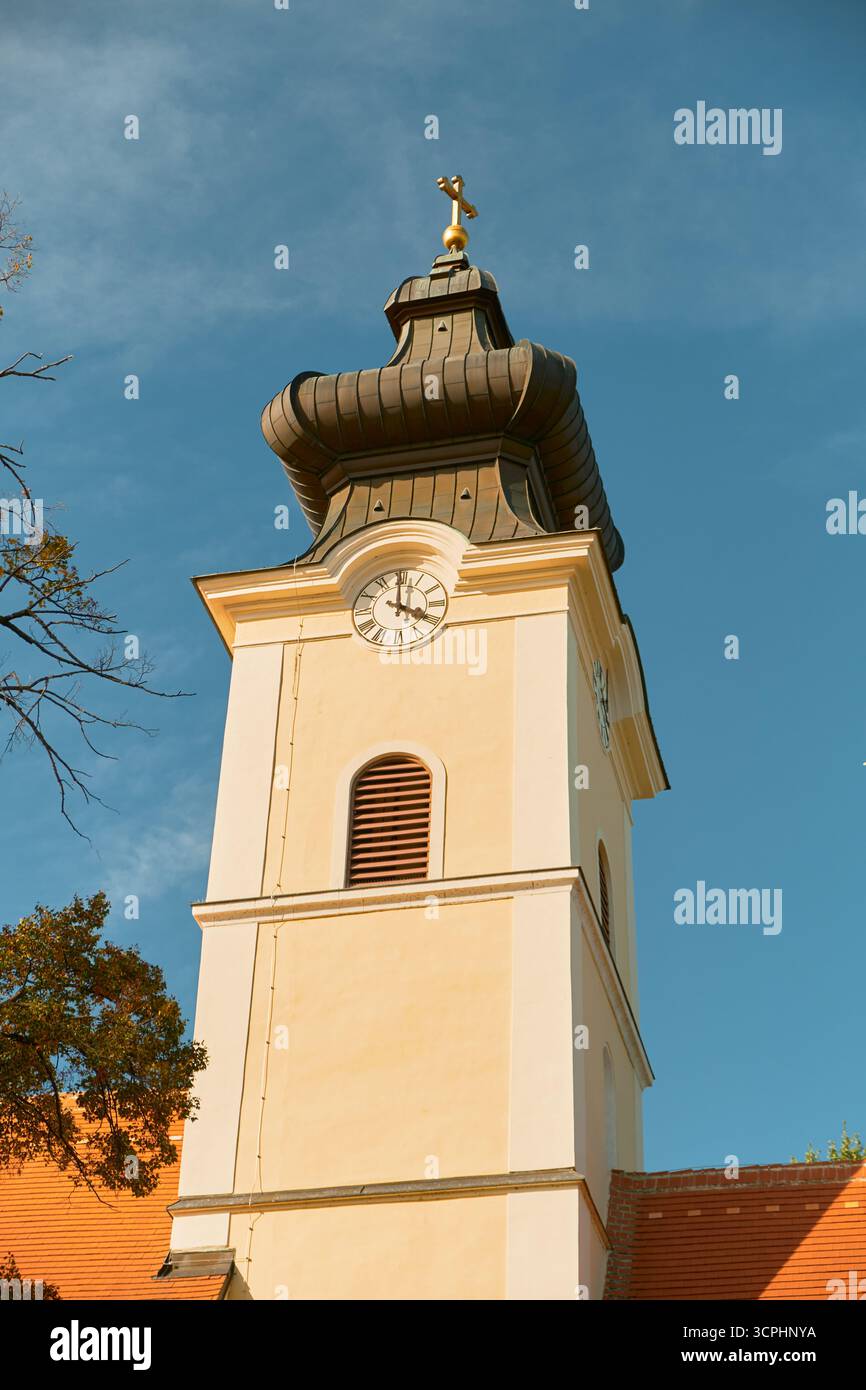 Vista ravvicinata della torre gialla della chiesa con cupola ornata, orologio e croce in cima. La tradizionale architettura religiosa europea si distingue contro la chiara Foto Stock