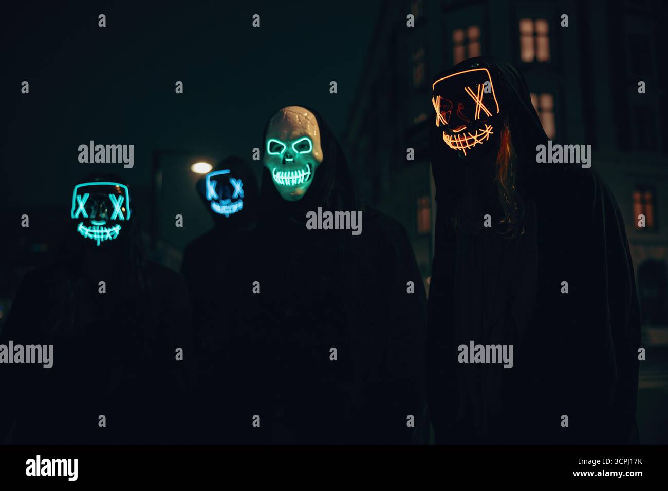 Gruppo di persone che indossano maschere luminose di notte in un ambiente urbano di strada, con abiti pseudonimi. Foto Stock