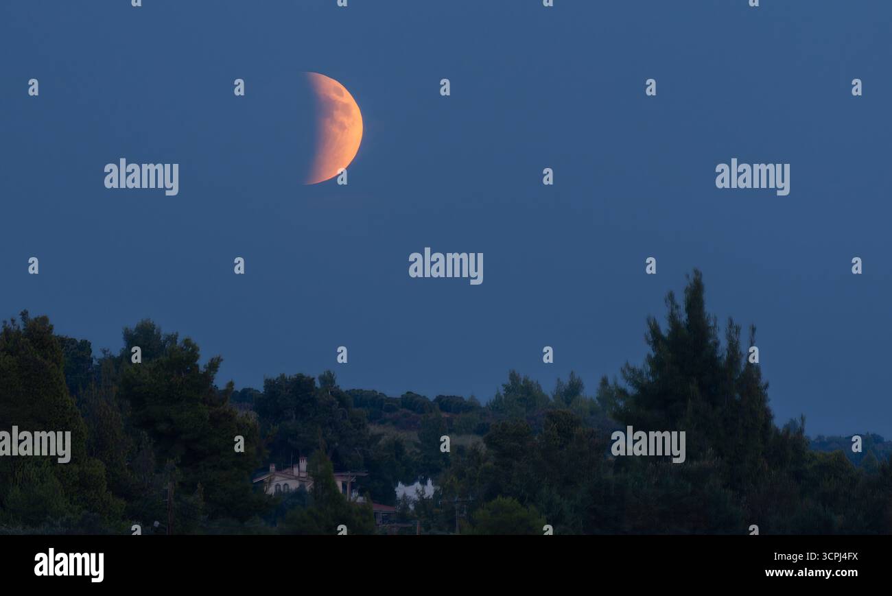 Questa accattivante immagine mostra una luna di sangue che illumina il cielo notturno, circondata da stelle scintillanti, evocando un senso di meraviglia e bellezza cosmica Foto Stock