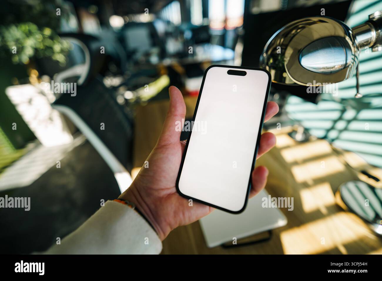Mockup smartphone spazio di lavoro ufficio dispositivo di tenuta. Primo piano della mano di una persona che tiene in mano uno smartphone moderno con schermo bianco bianco vuoto in un momento di disprezzo Foto Stock