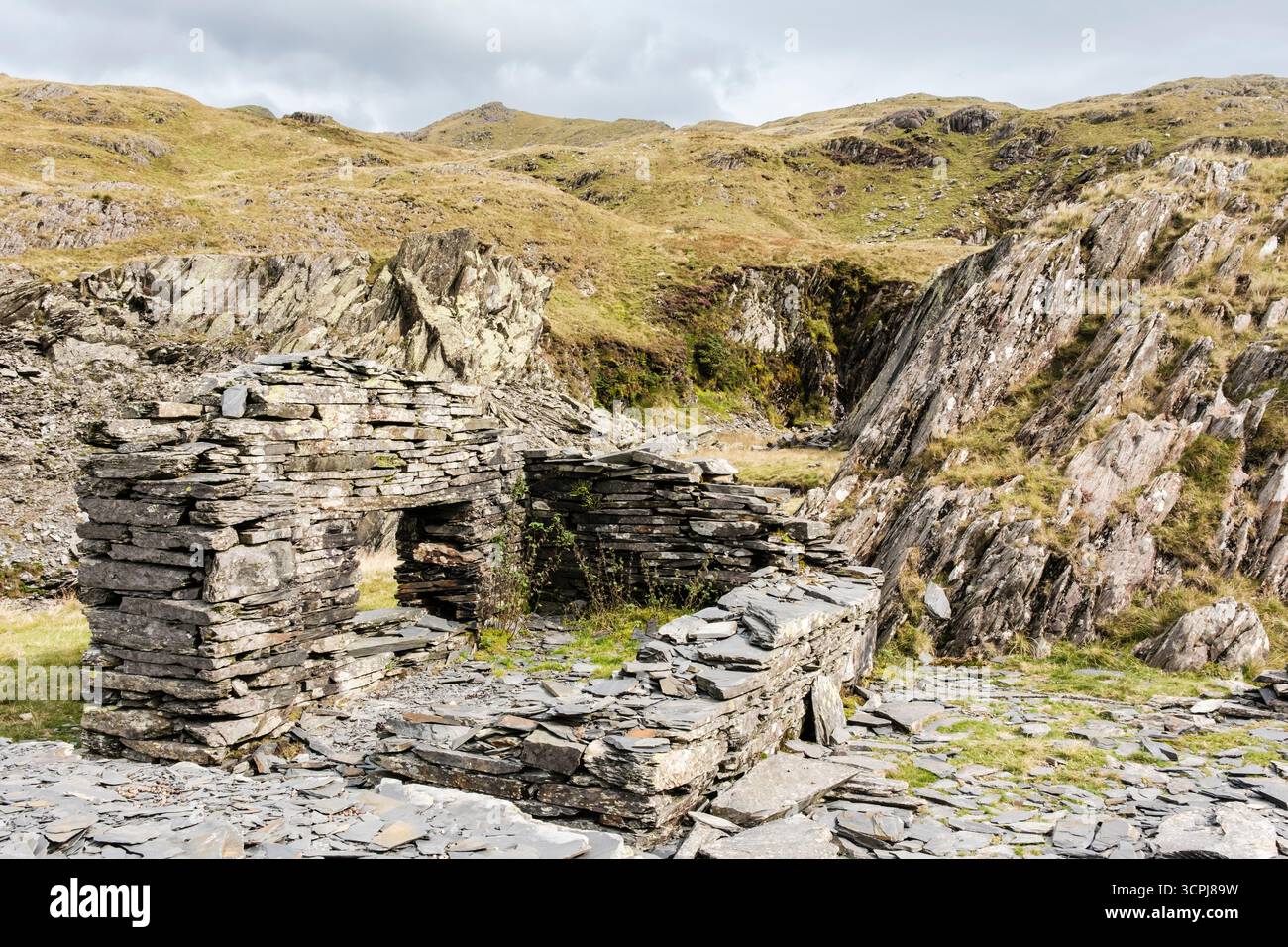 Vecchia cava di ardesia abbandonata sul Miners Track da Rhyd DDU a Bwlch Cwm Llan con la cresta sud di Snowdon in lontananza in Snowdonia. Galles del nord, Regno Unito Foto Stock