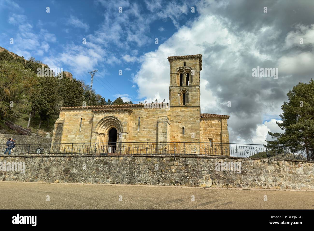 Storica chiesa romanica con campanile in pietra e porta ad arco contro un cielo nuvoloso. Foto Stock
