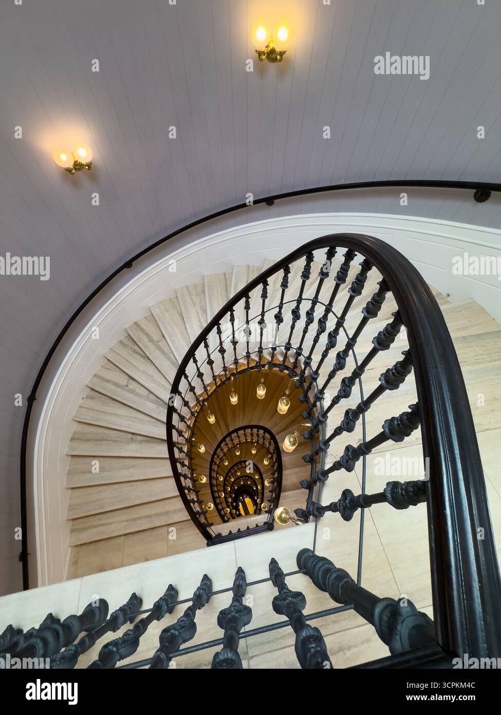 Ringhiere in ferro ornate circondano una scala a spirale illuminata che crea un'altezza e una profondità eleganti Foto Stock