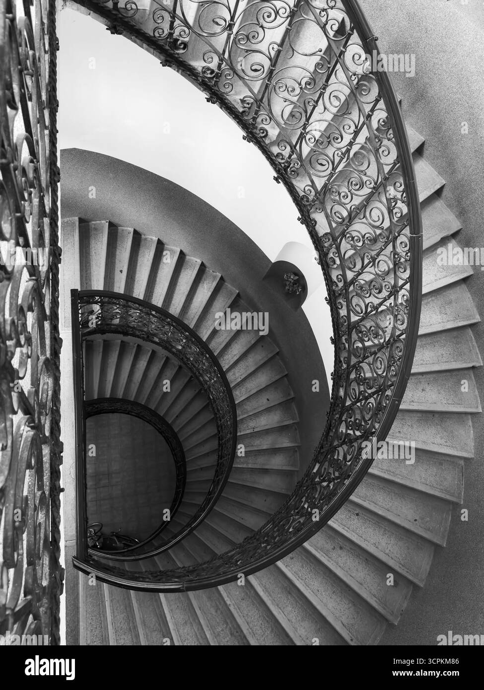 Scala a chiocciola con vista monocromatica e ringhiera decorativa in ferro battuto. Le linee circolari con ombre profonde creano una texture architettonica spettacolare, un senso di eleganza misteriosa in salita Foto Stock