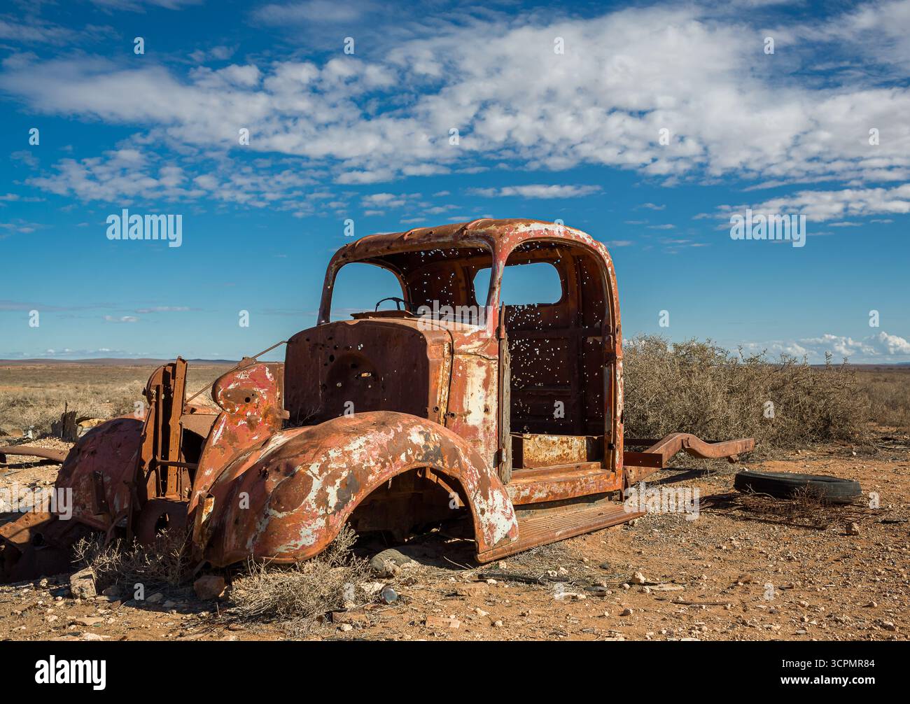 Rusty, camion abbandonato con buchi di proiettile nelle Flinders Ranges, Australia meridionale, sullo sfondo di un paesaggio arido e arido e arbusti sparsi. Foto Stock