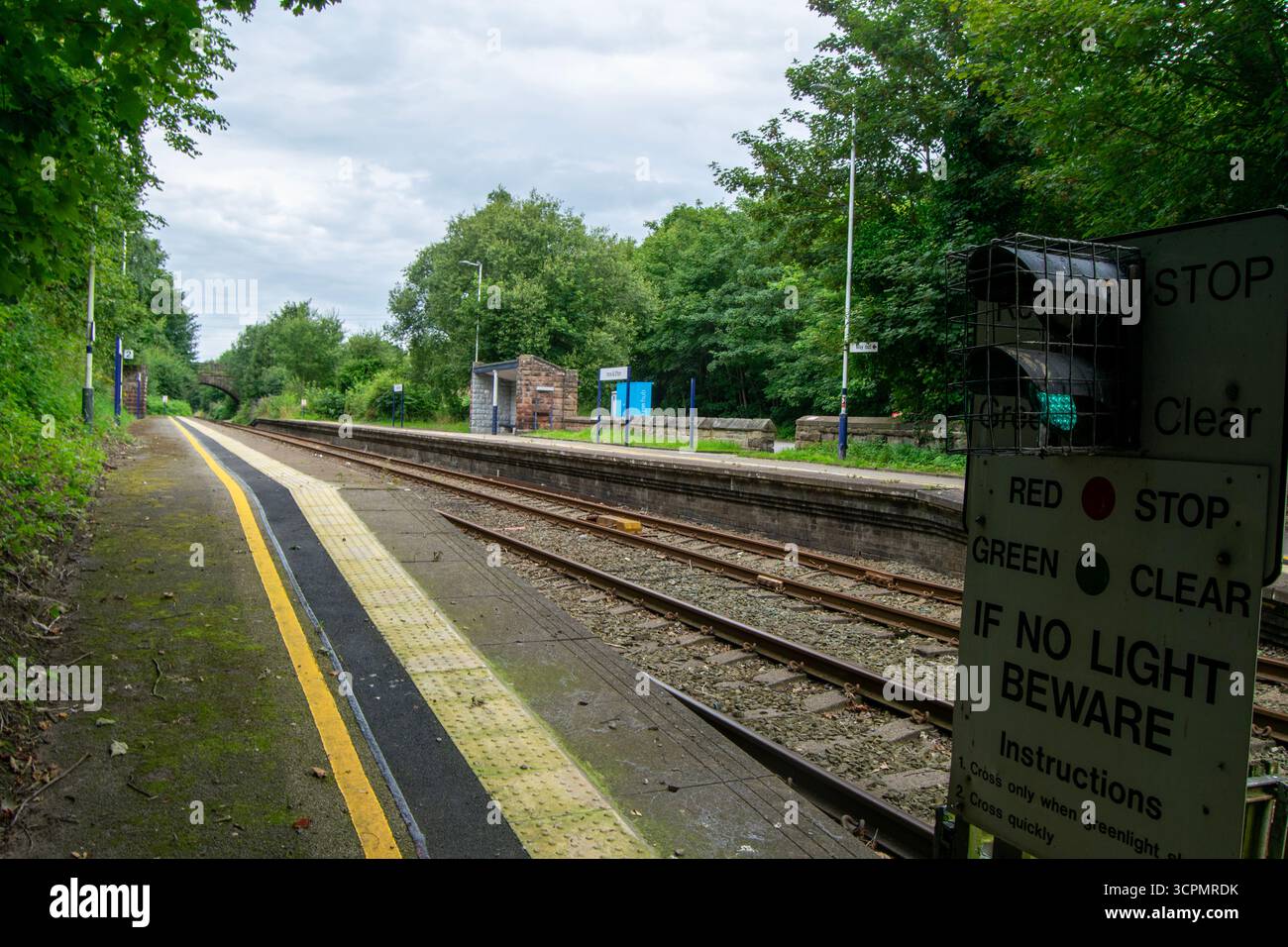 Vista tranquilla della stazione ferroviaria di Ince ed Elton, Cheshire, con piattaforme, binari e ripari originali in pietra circondati da vegetazione lussureggiante. Foto Stock