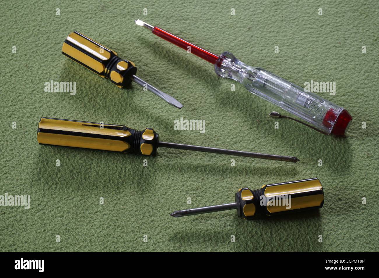Cacciavite phillips giallo, cacciavite a tre alette e penna di prova bianca rossa su sfondo verde. Apparecchiature per la riparazione elettrica. Foto Stock