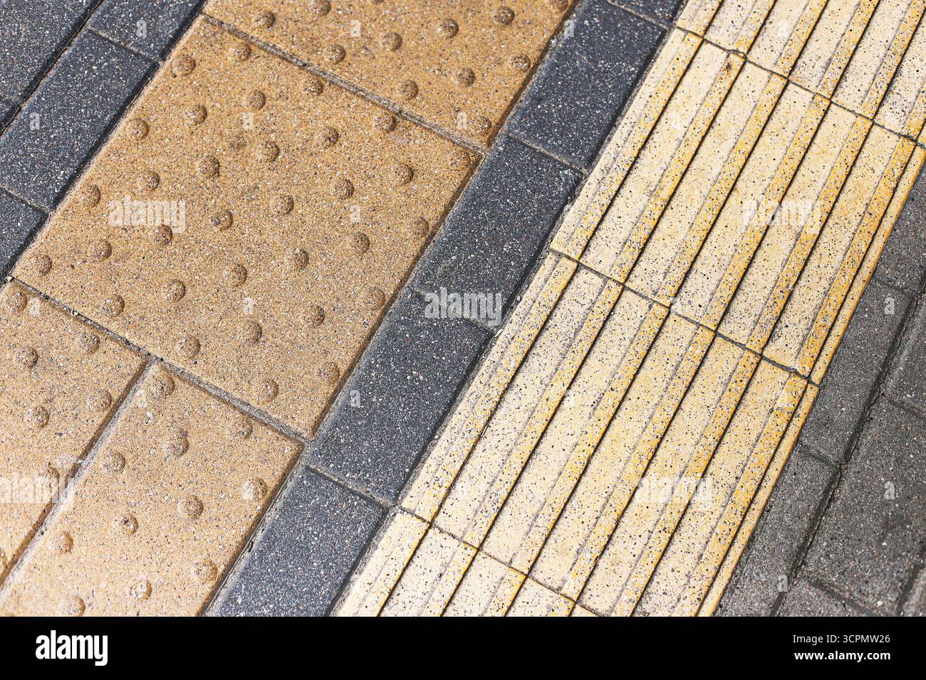 Pavimentazione tattile sul marciapiede urbano. Struttura di sicurezza per pedoni ciechi. Piastrelle gialle e marroni con linee guida. Foto Stock