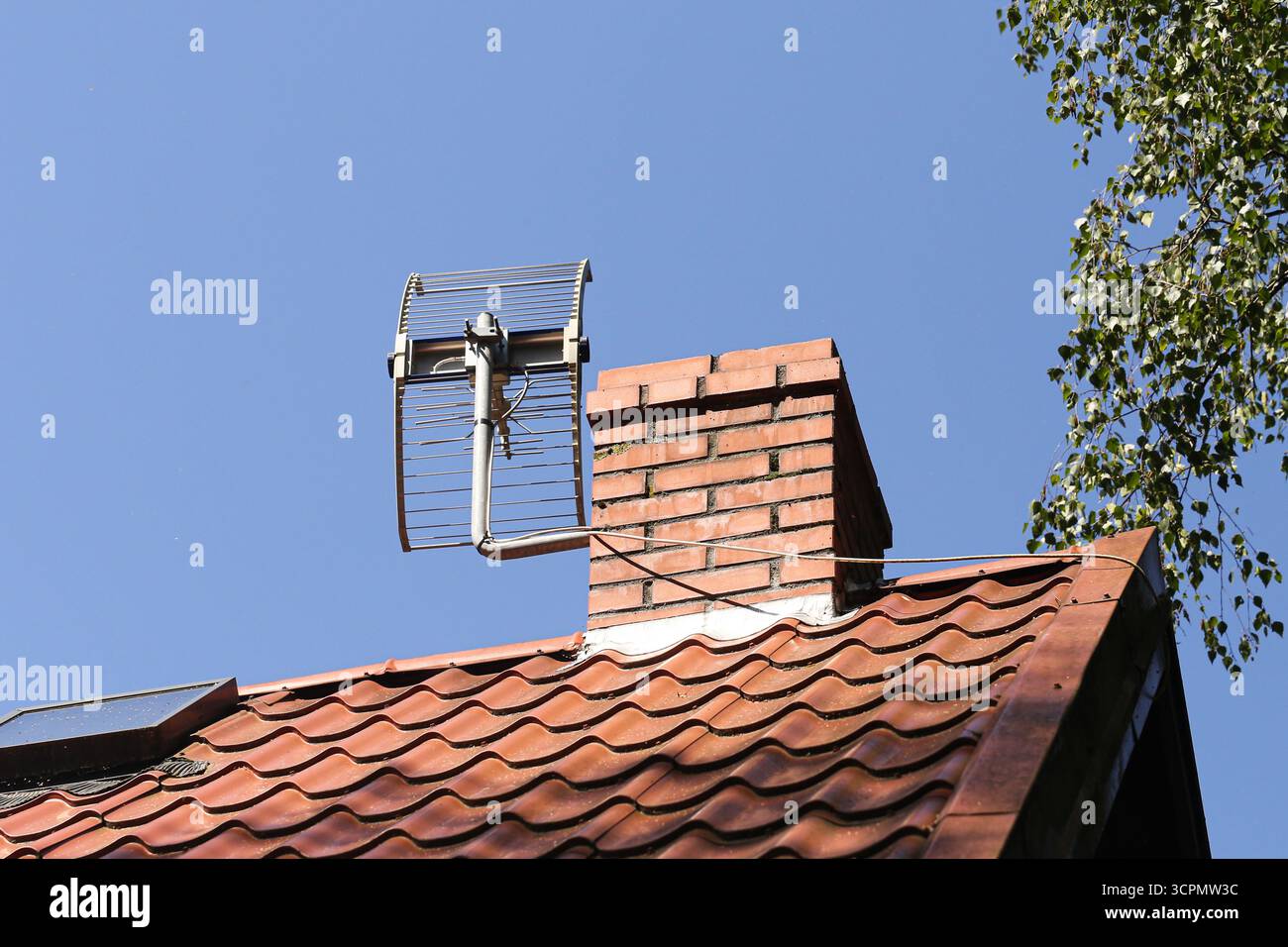 Tetto con piastrelle rosse e antenna sulla parte superiore. Sfondo blu chiaro del cielo. Dettagli di costruzione della casa con apparecchiature di comunicazione. Vista esterna dell'edificio urbano Foto Stock