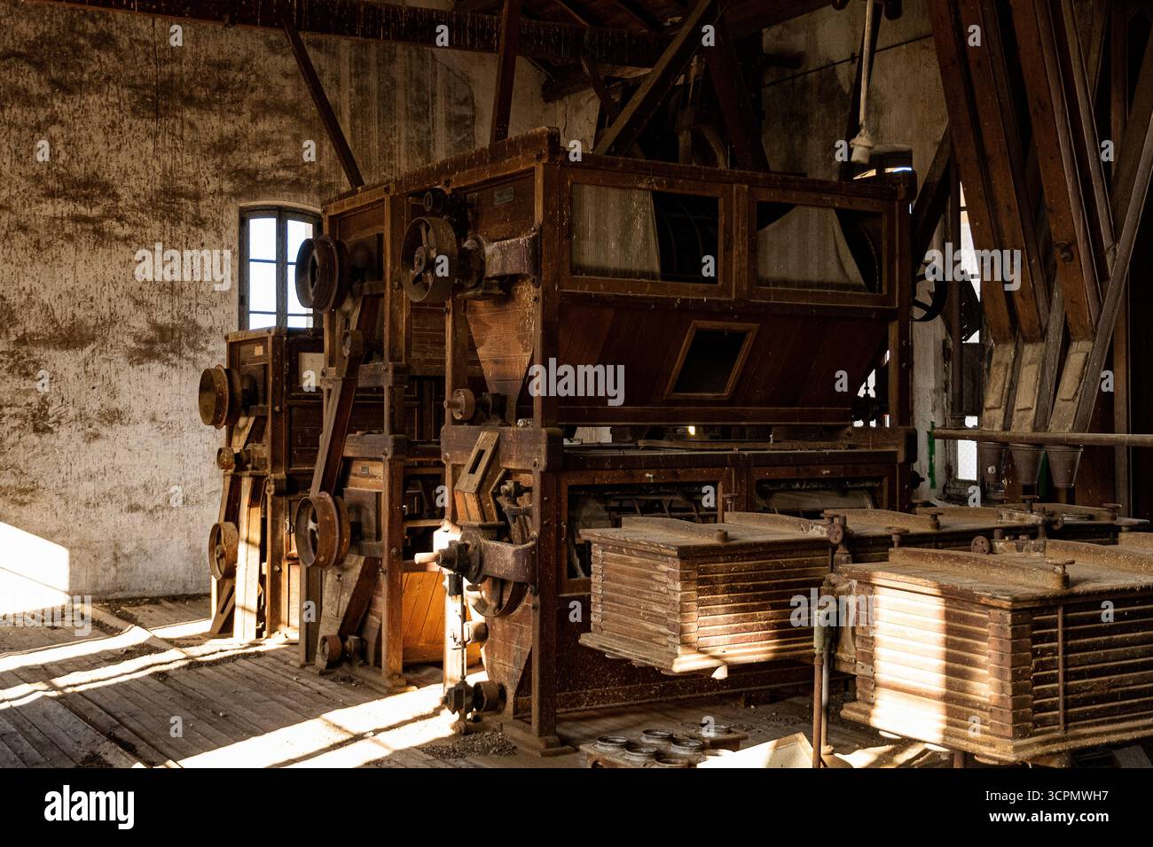 I vecchi macchinari si trovano inattivi in un vecchio magazzino illuminato dal sole, che mostra l'artigianato e la storia d'epoca. Foto Stock