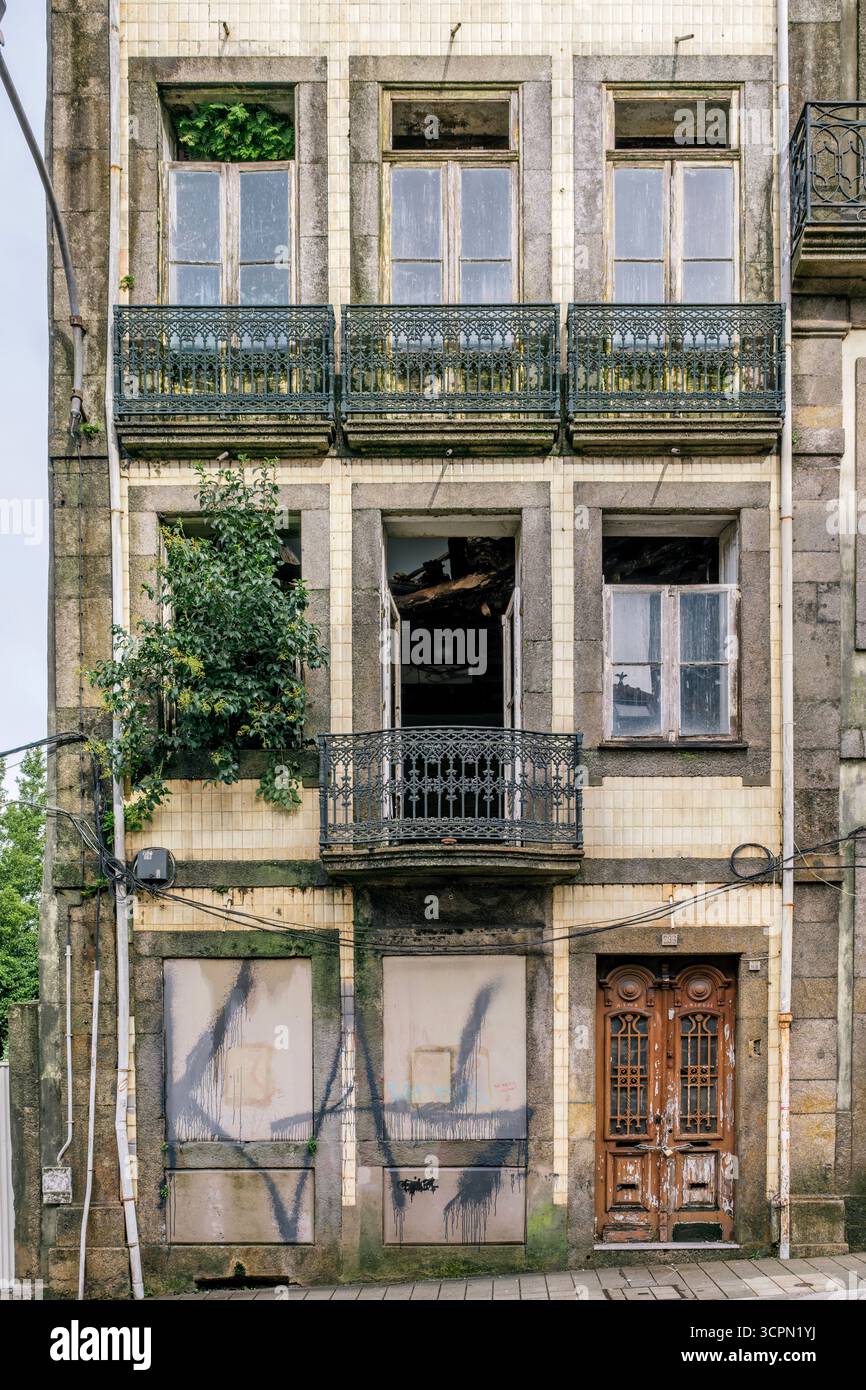 Facciata decadente di un edificio urbano abbandonato con balconi in ferro ornati a Porto. Degrado urbano, architettura residenziale, negligenza, texture grintose Foto Stock