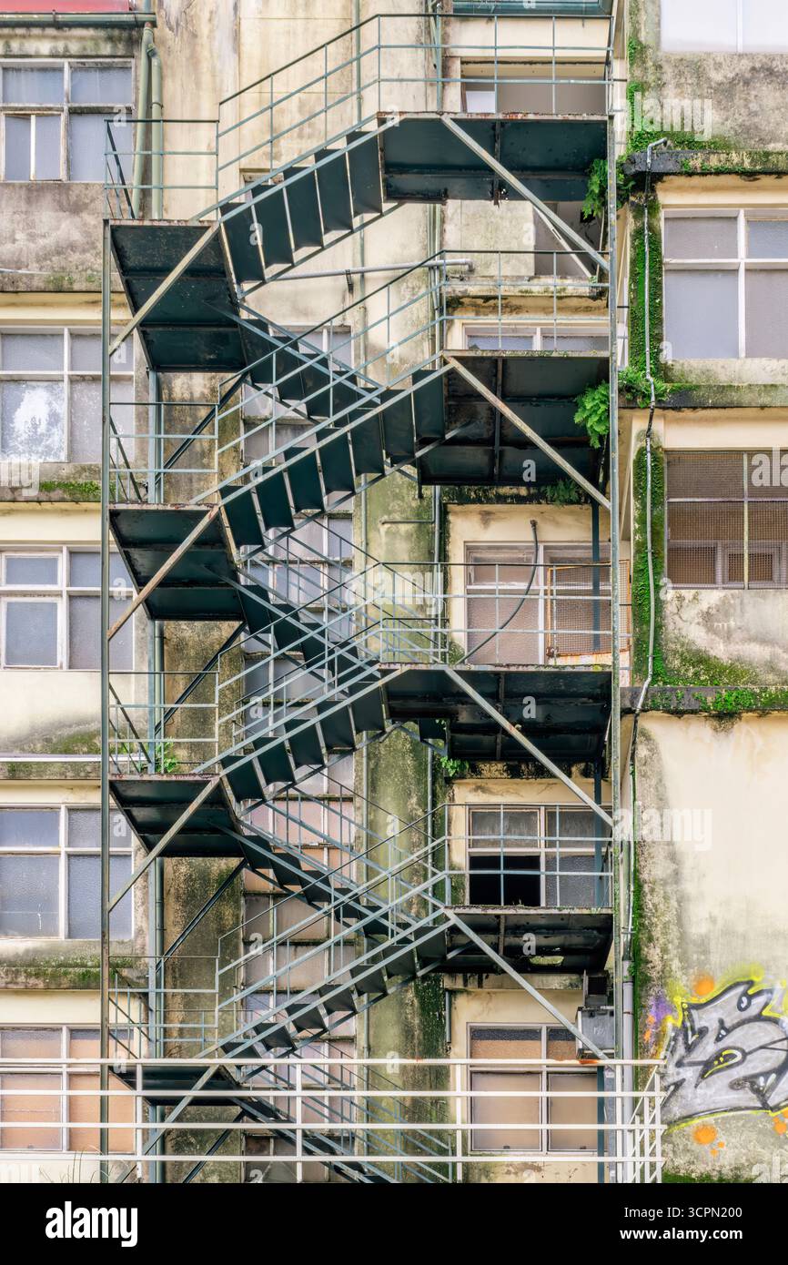 Rusty Exterior Metal Escape Staircase zigzagando lungo Una grungy facciata di Un edificio abbandonato. Degrado urbano, architettura industriale, texture grintose Foto Stock