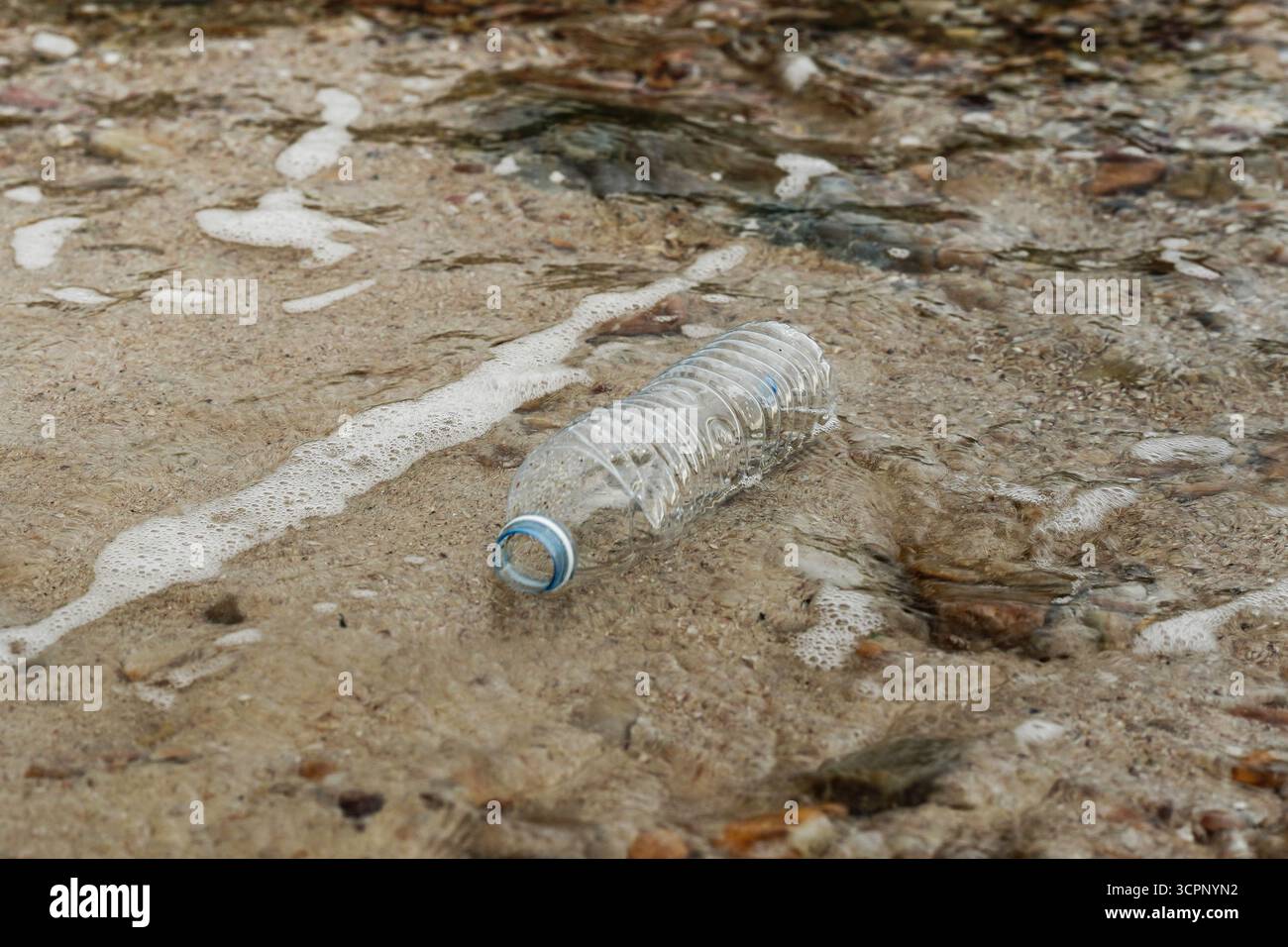 Bottiglia di plastica gettata adagiata su una spiaggia sabbiosa, simbolo dell'inquinamento ambientale e dei rifiuti oceanici. Foto Stock