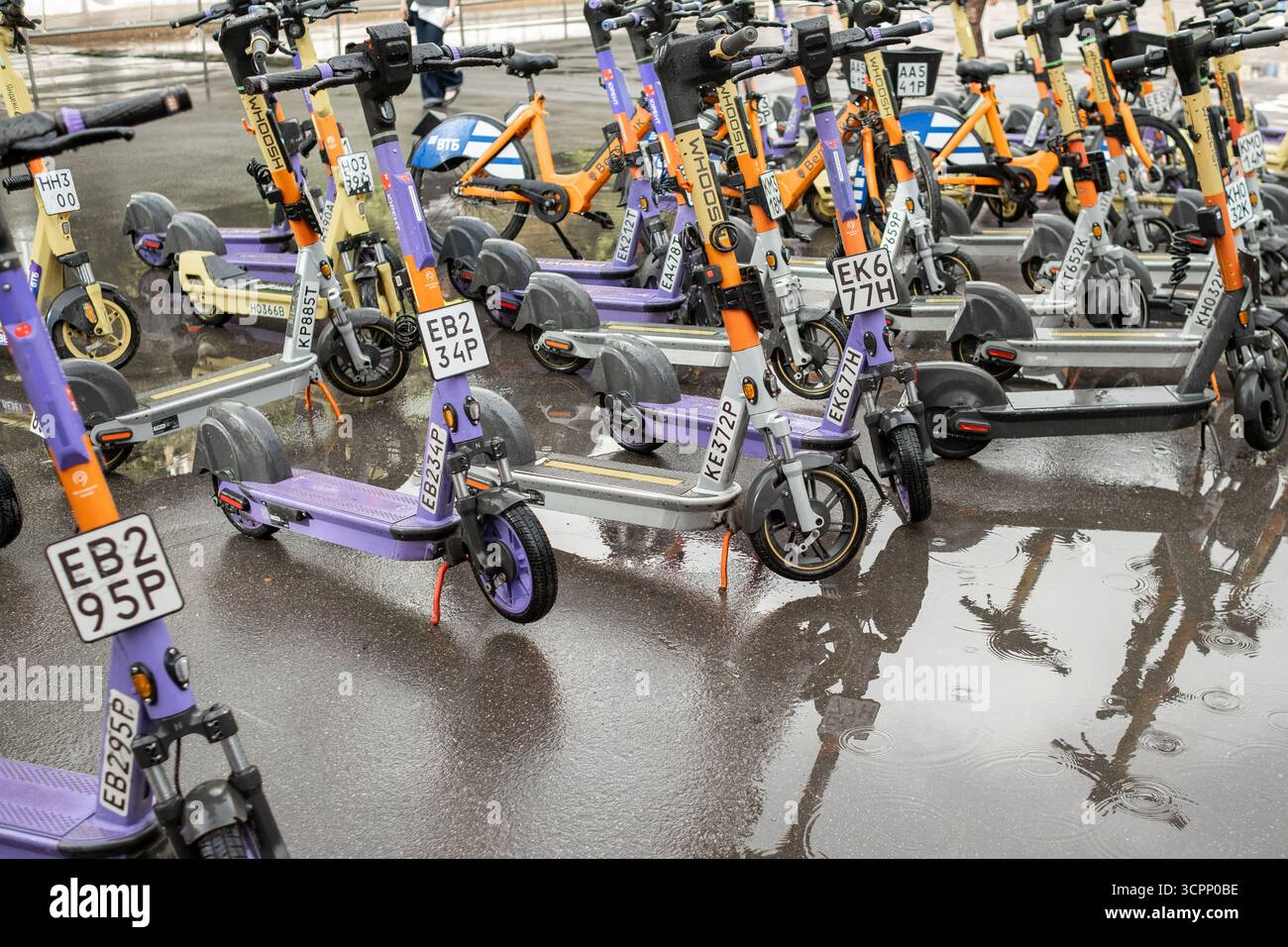 25 agosto 2025, Mosca, Russia. Diversi scooter elettrici sono parcheggiati a caso accanto a una marionetta su un marciapiede bagnato, che mostra il tempo piovoso Foto Stock