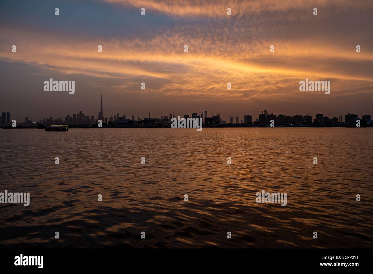 Guarda un video dello skyline panoramico di Dubai al tramonto con cielo dorato e increspature d'acqua, vista panoramica dal porto di Creek con barche e yacht Foto Stock