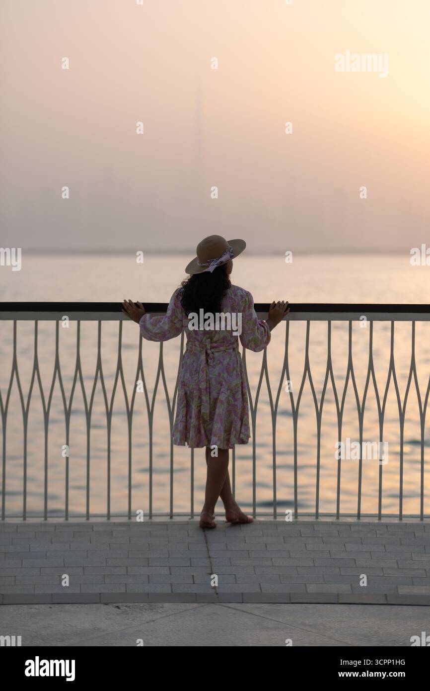 Giovane donna turistica che cammina sul lungomare al porto di Dubai creek con lo skyline del centro di Dubai sullo sfondo Foto Stock