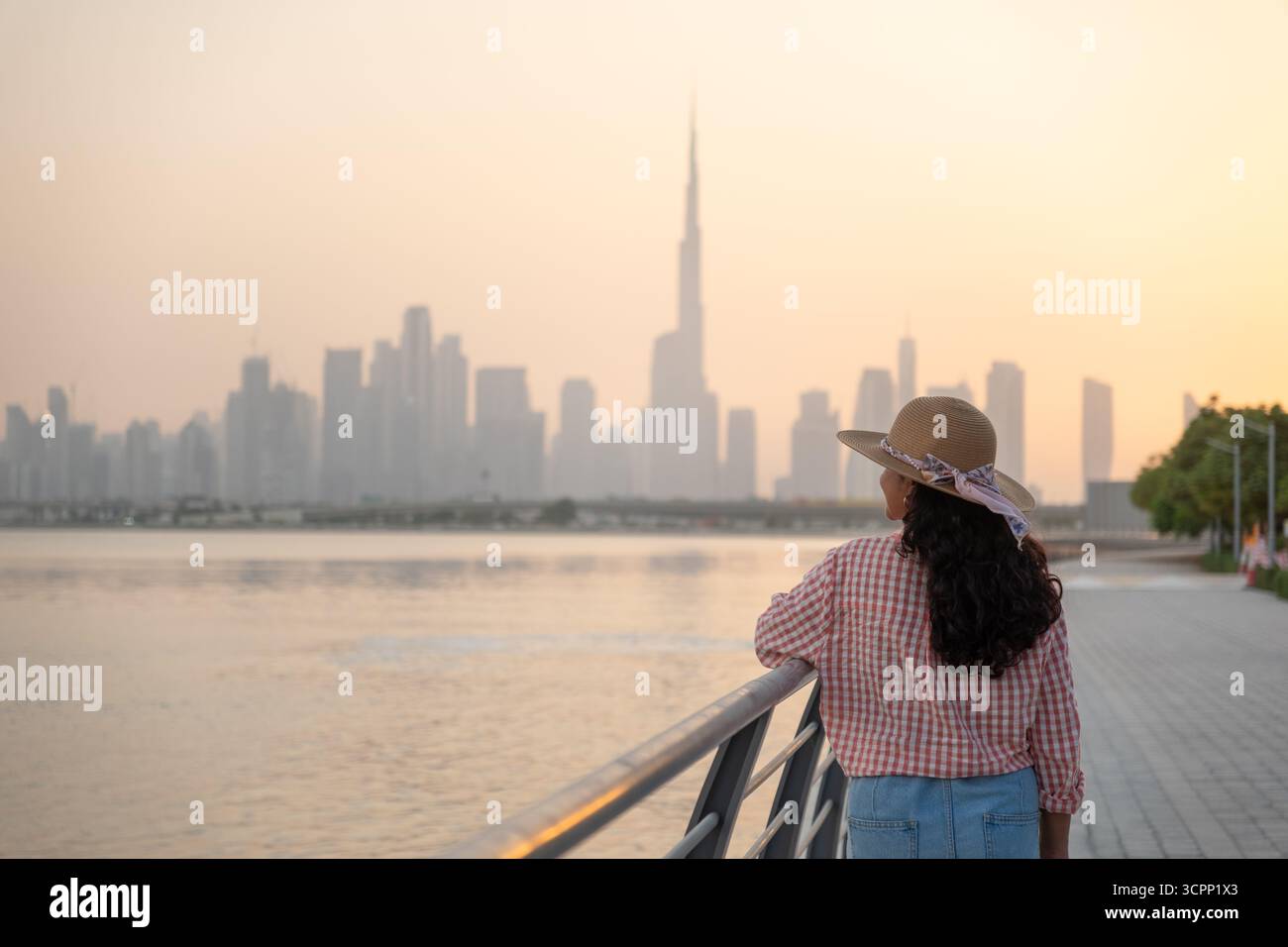 Giovane donna elegante che guarda la silhouette dello skyline di Dubai al tramonto, la lussuosa posizione sul lungomare di Dubai e le opportunità di investimento immobiliare premium Foto Stock