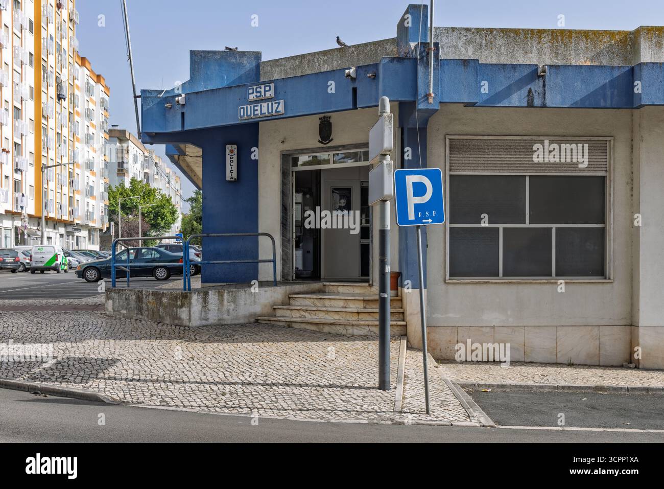 Una foto esterna di una stazione di polizia blu e bianca a Queluz, Portogallo. Il cartello "PSP Queluz" è visibile sopra l'ingresso, con un'auto parcheggiata e una Foto Stock