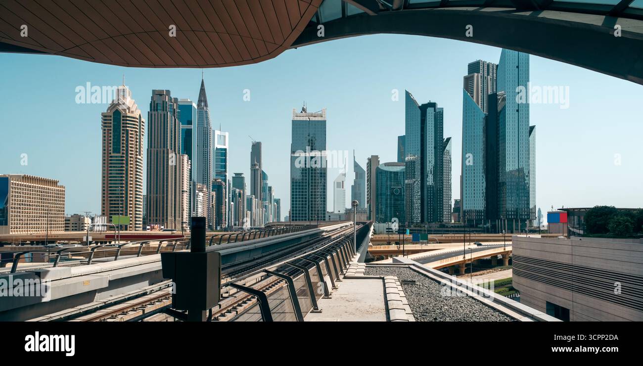 Moderno paesaggio urbano di Dubai con alti edifici in vetro, vista sulla piattaforma della metropolitana, binari ferroviari sopraelevati e futuristici grattacieli Foto Stock