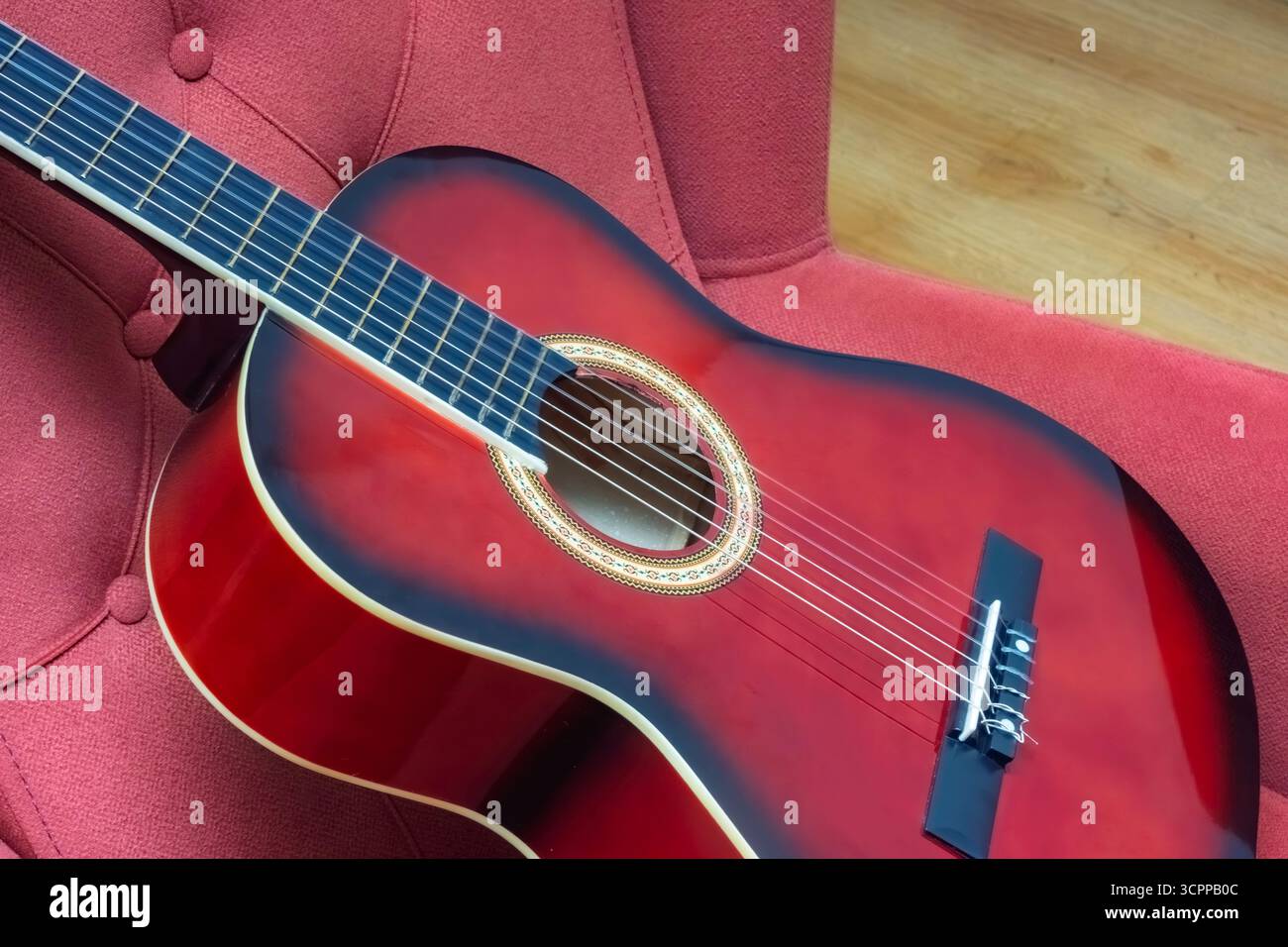 Primo piano di una chitarra acustica rossa appoggiata su una lussuosa sedia. Questa straordinaria immagine mette in risalto la maestria e la bellezza della chitarra. Foto Stock