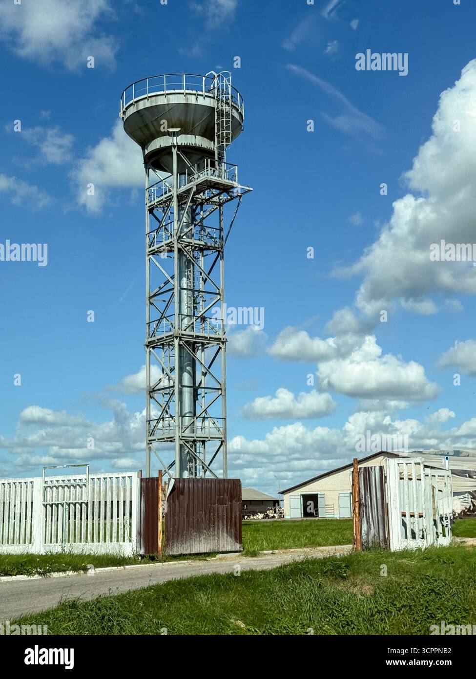 Vecchia torre d'acqua rustica racchiusa da una recinzione, che mostra l'architettura industriale d'epoca e le infrastrutture rurali sotto cieli limpidi - Immagine stock catturata con smartphone
