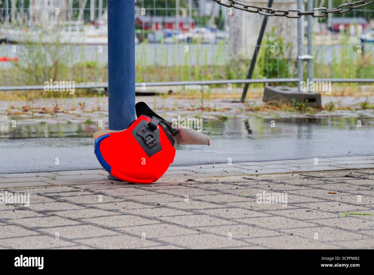 Un elmetto rosso da pompiere giace capovolto vicino a un palo d'acciaio sull'asfalto e le cinghie interne e la visiera sono visibili mentre la carreggiata vuota lo suggerisce Foto Stock