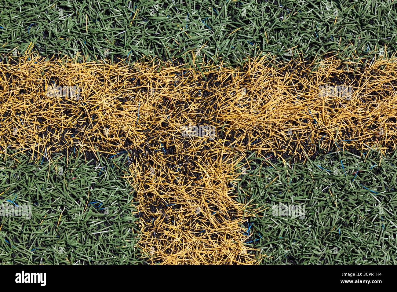 Primo piano di linee intersecanti verniciate a spruzzo giallo sotto forma di T su erba verde artificiale su campi sportivi a uso multiplo. Foto Stock