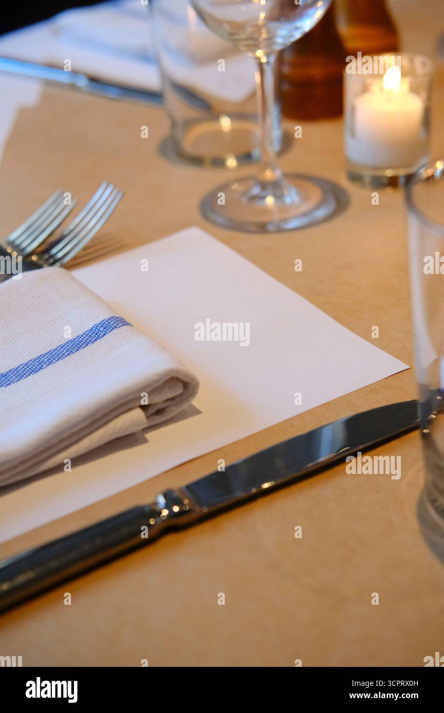 Elegante tavolo con coltello e forchette, carta bianca come mockup e tovagliolo a strisce piegato Foto Stock