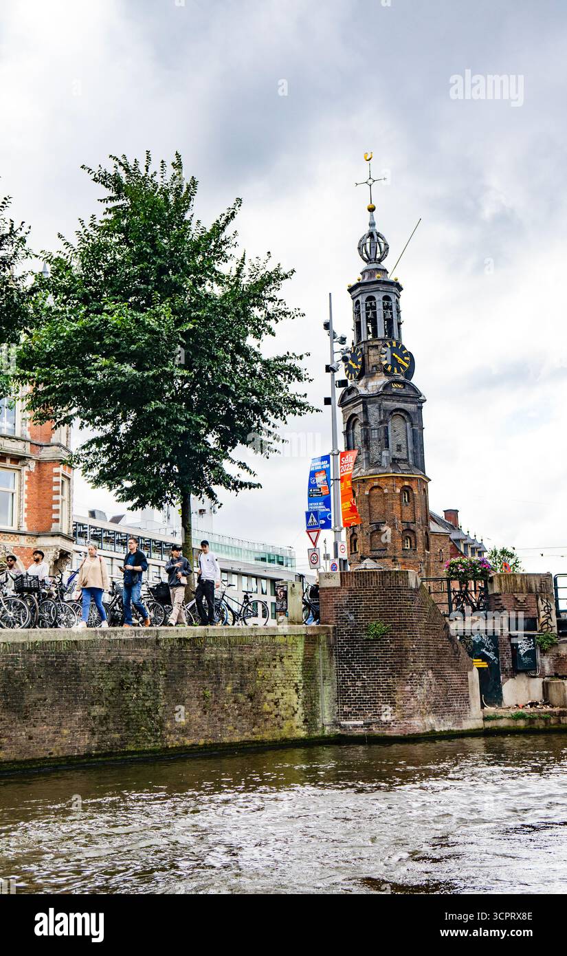 Torre dell'orologio su un canale con persone e biciclette ad Amsterdam, Paesi Bassi Foto Stock
