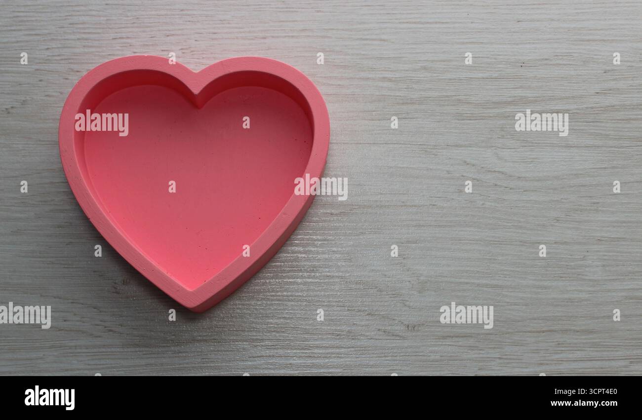 Una scatola a forma di cuore rosa con bordi alti si staglia su una tavola di legno testurizzato di quercia bianca con spazio per copie Foto Stock