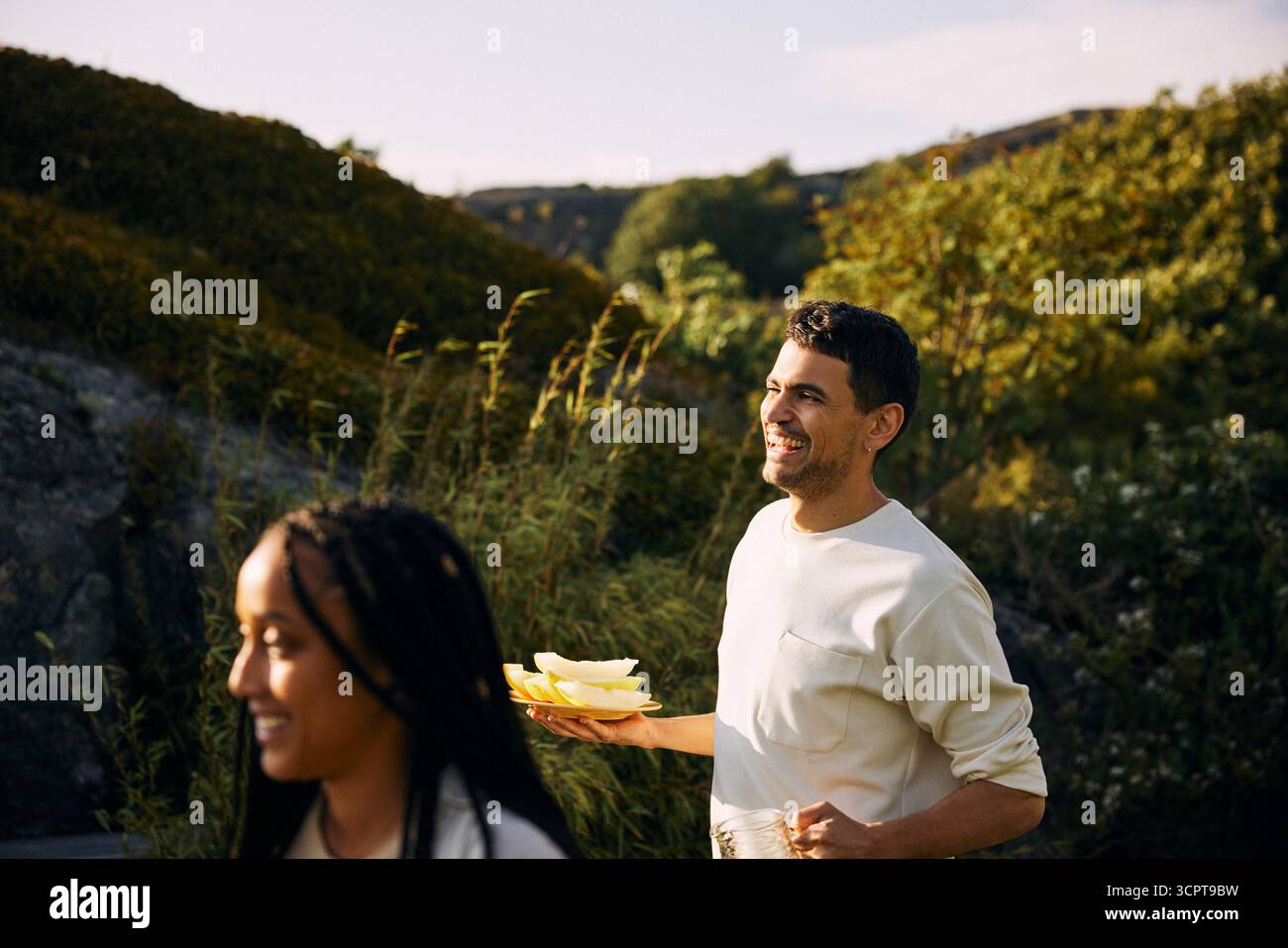 Uomo felice con melone in mano che cammina nel cortile posteriore in giornata di sole Foto Stock