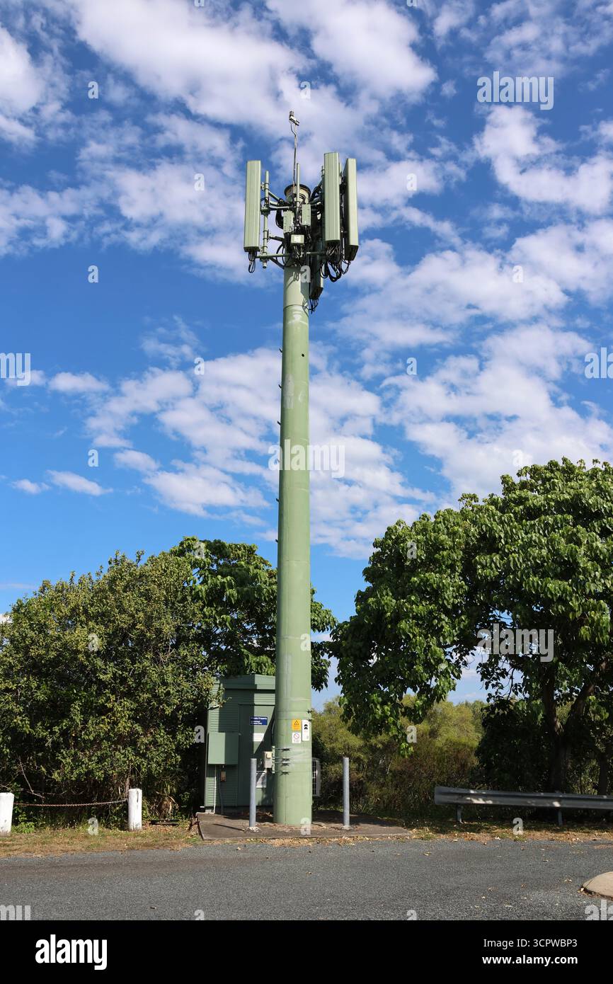 Torre delle telecomunicazioni di fronte agli alberi con un cielo blu con nuvole bianche sparse Foto Stock