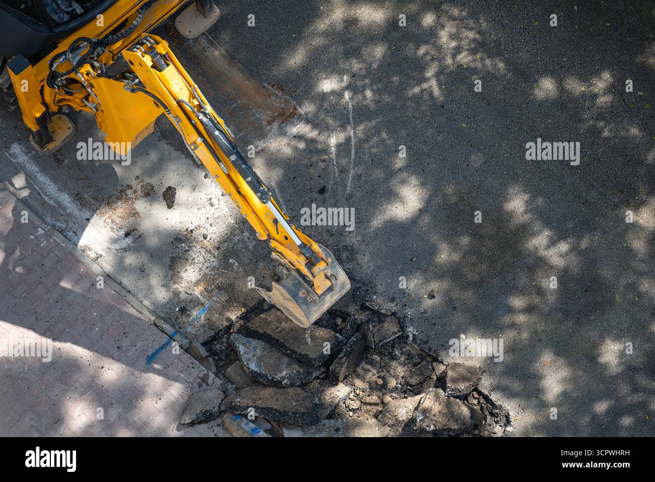 Vista dall'alto dell'escavatore giallo che scava asfalto per la manutenzione stradale Foto Stock
