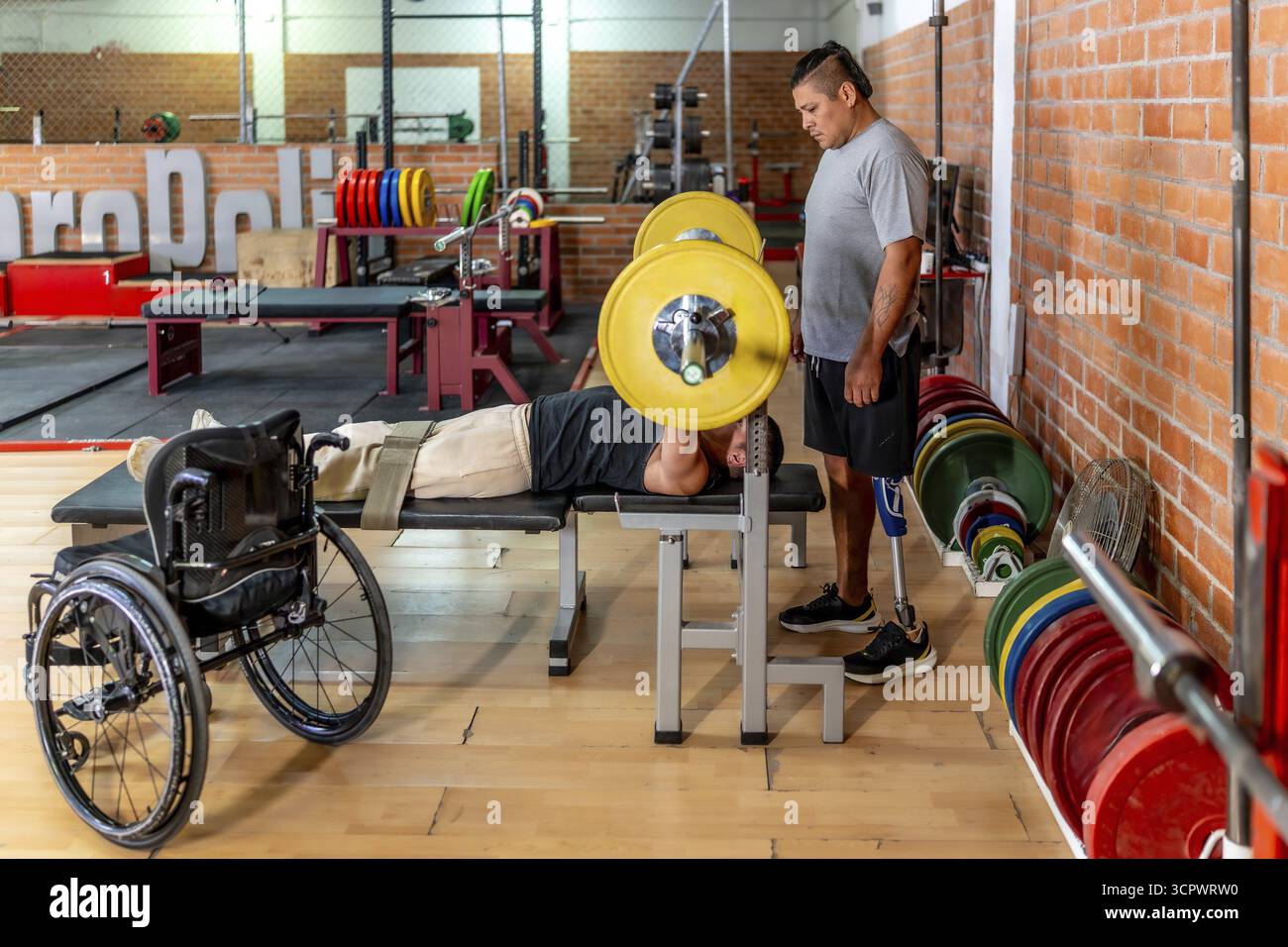 Due uomini determinati si allenano in una panchina di ginecologia premendo i pesi mentre il suo compagno di squadra con una gamba protesica si sostiene mostrando forza adattiva A. Foto Stock