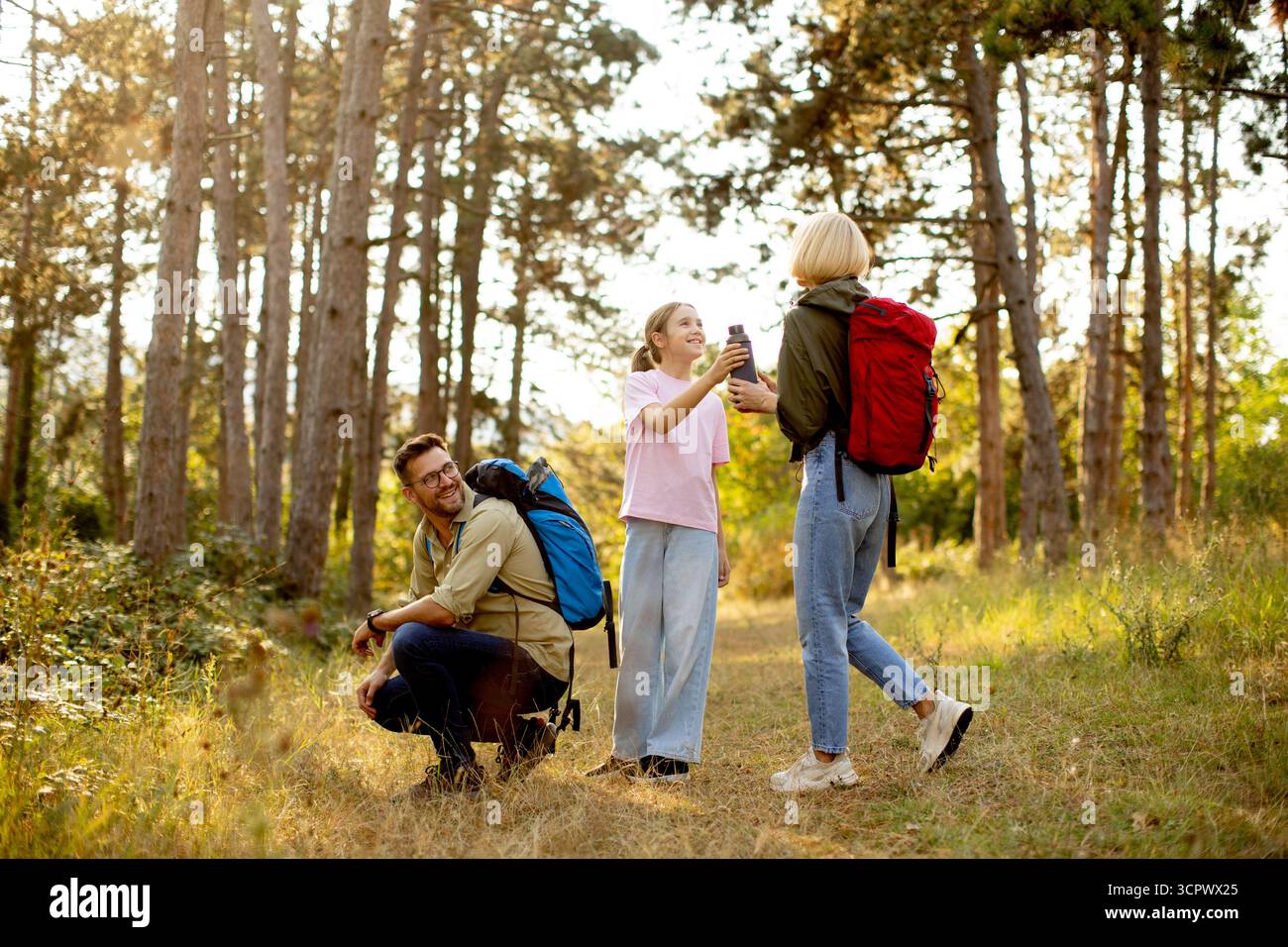 Una famiglia sta camminando su un sentiero soleggiato in una foresta. Due membri stanno chattando mentre un bambino scatta una foto. Sono circondate da alti alberi e vibra Foto Stock