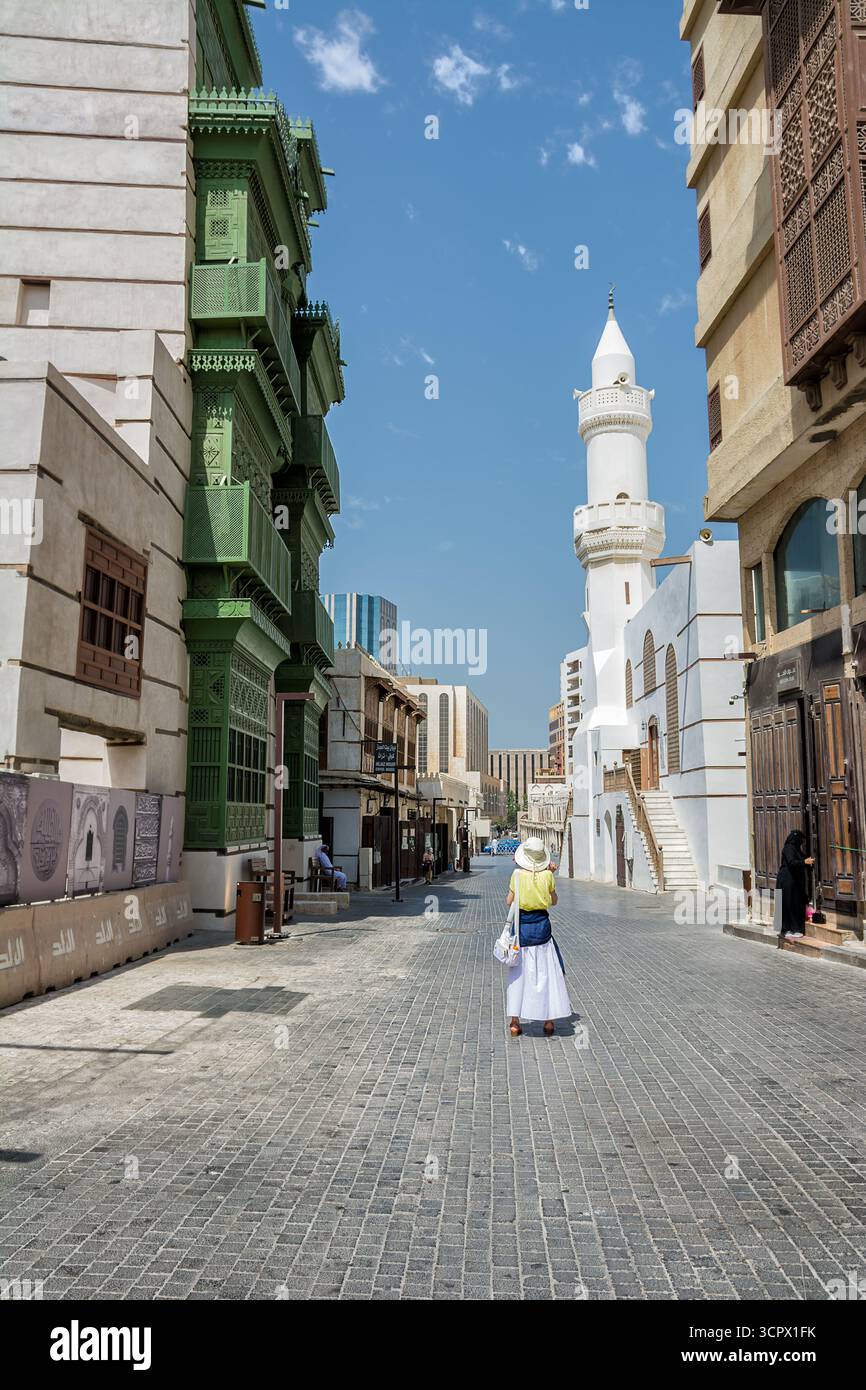 Jeddah, Arabia Saudita - 20 aprile 2025: Turista europeo che cammina nelle vecchie strade di al Balad Jeddah Arabia Saudita con finestre tradizionali e moschea Foto Stock