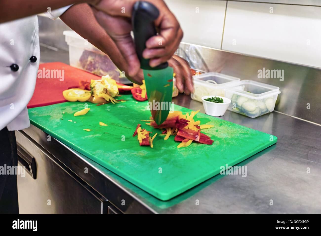 Lo chef africano cucina le mani da vicino, tagliando le verdure con un coltello nella cucina del ristorante sul tagliere Foto Stock