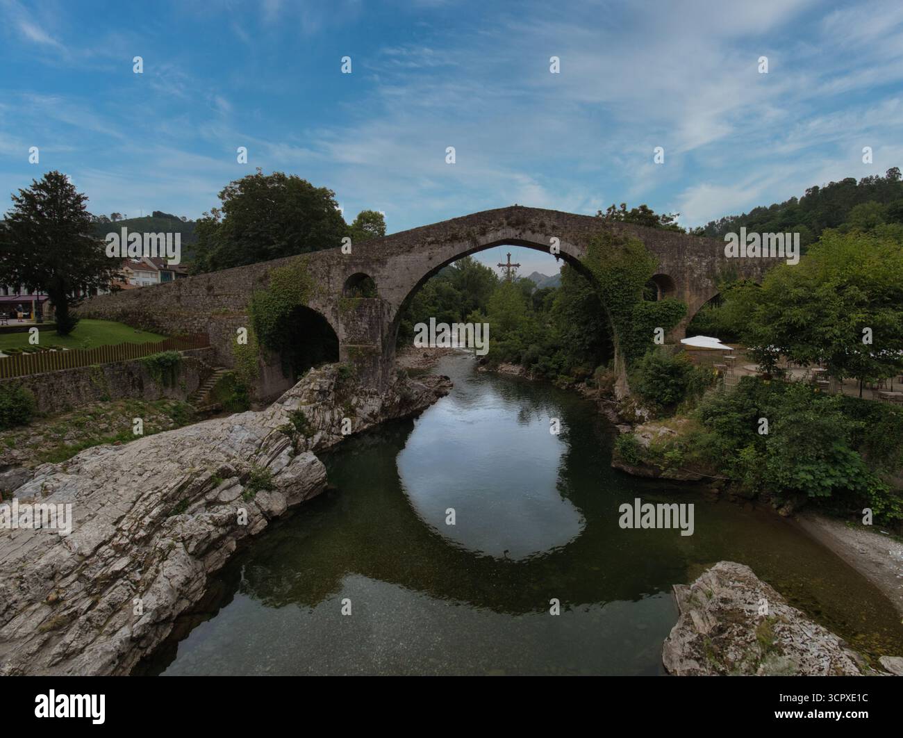 Storico ponte medievale di pietra sul fiume - pittoresco ponte di pietra ad arco singolo con spessa edera che attraversa un fiume tranquillo e riflettente circondato da lussureggianti giardini Foto Stock