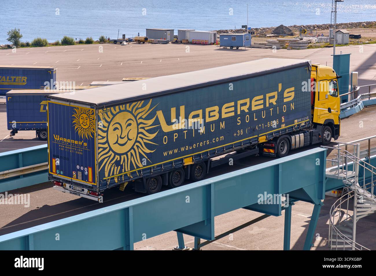 Trelleborg, Svezia; 23 settembre 2025: Un camion Renault giallo con rimorchio blu Warerger e logo giallo del sole sale sulla rampa per il traghetto presso Th Foto Stock