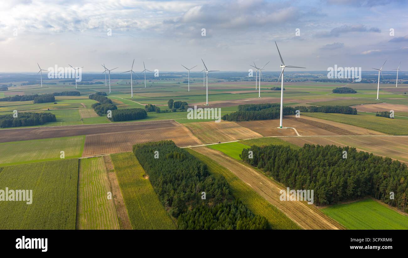 Vista aerea panoramica delle turbine eoliche sui campi agricoli verdi e marroni, con alberi sparsi e un cielo parzialmente nuvoloso che getta ombre morbide. Foto Stock