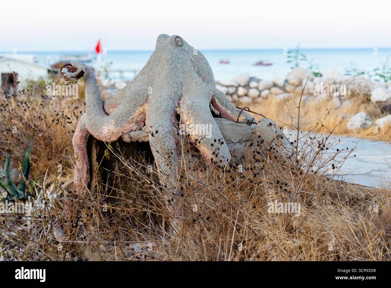 Una statua di polpo su una spiaggia, in primo piano di erba secca, oceano e cielo sullo sfondo. Foto Stock