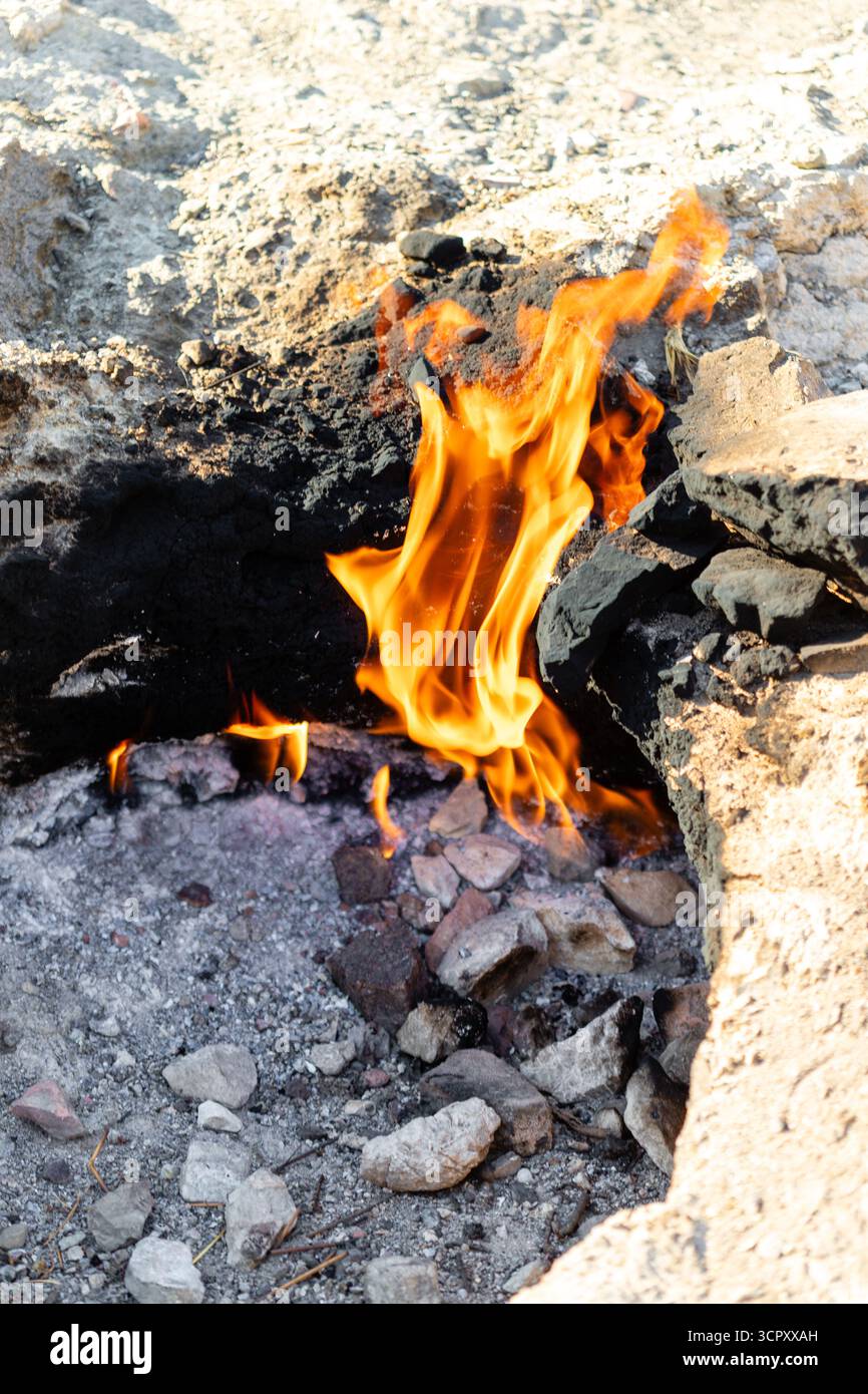 Fiamme che bruciano in una fossa rocciosa con ambienti scuri e inceneriti e formazioni rocciose di colore chiaro. Foto Stock