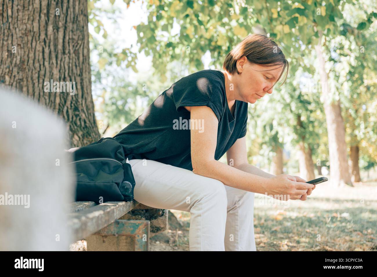Donna adulta matura seduta su una panchina del parco e che usa un telefono cellulare in una giornata di sole. Messa a fuoco selettiva. Foto Stock