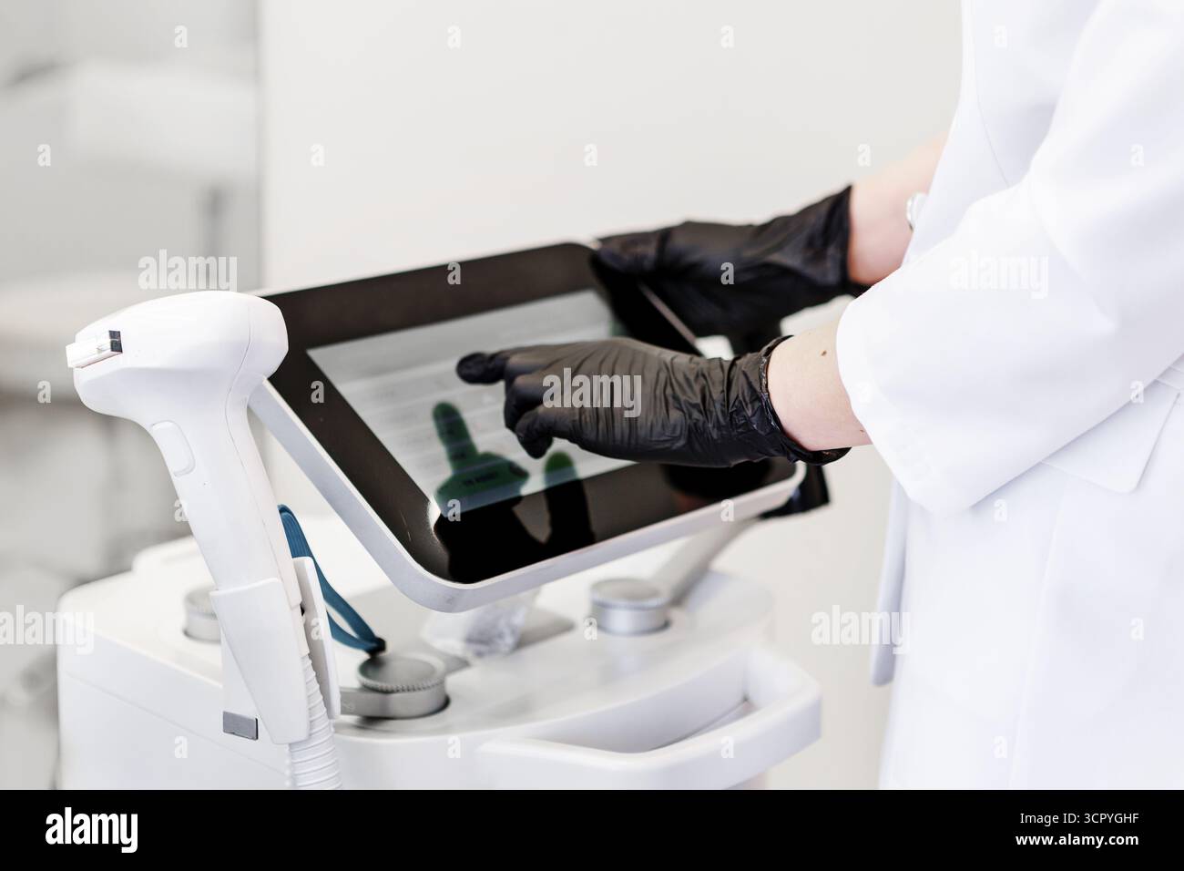 Cosmetologo in camice bianco e guanti neri che utilizza il pannello di controllo touchscreen della moderna macchina laser in un centro di bellezza, attrezzature estetiche professionali Foto Stock
