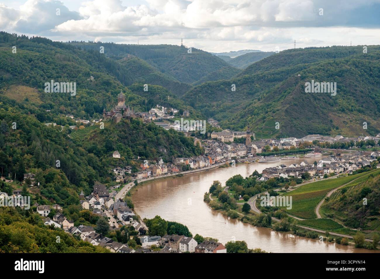 Panorama della città di Cochem e della Mosella con il castello e gli alberi verdi d'autunno sotto il cielo nuvoloso, Germania Foto Stock