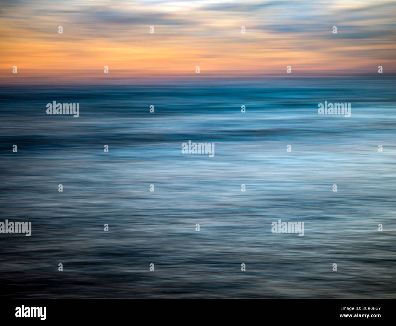 I colori si fondono magnificamente mentre il sole tramonta sull'Oceano Atlantico a Huelva, in Spagna. L'esposizione lunga cattura il movimento delle onde e del cielo. Foto Stock