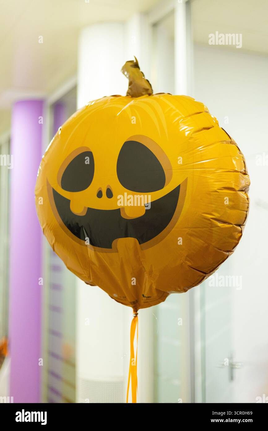 Un palloncino arancione rotondo simile a una zucca presenta un volto sorridente ed è galleggiante all'interno, creando un'atmosfera festosa per le celebrazioni di Halloween. Foto Stock