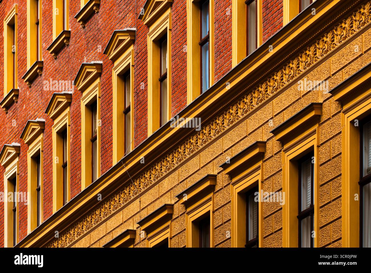 Facciata storica con mattoni rossi e dettagli decorativi in stucco giallo alla luce calda del sole Foto Stock
