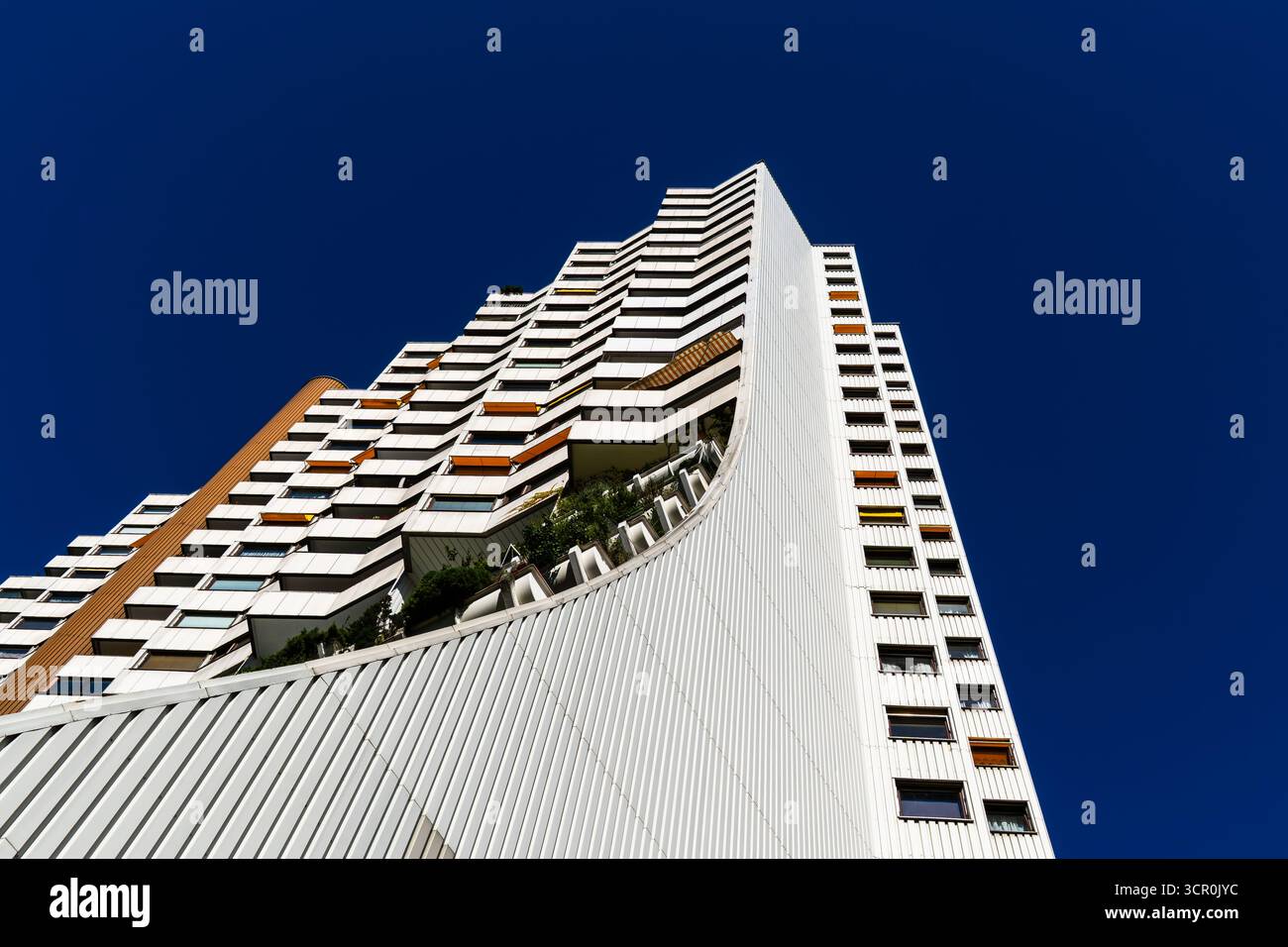 Moderno ed alto edificio residenziale con facciata curva e terrazze verdi sotto un cielo blu profondo e limpido Foto Stock